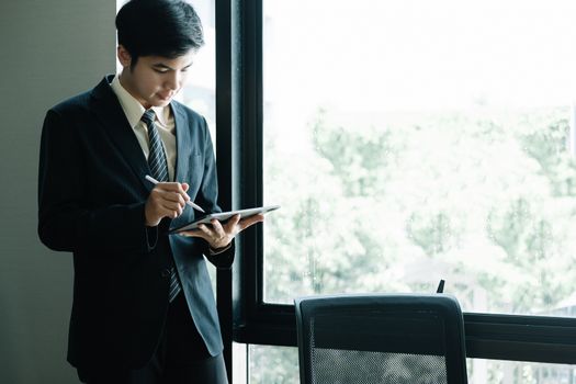 Young Asian Businessman Standing and using tablet at office.