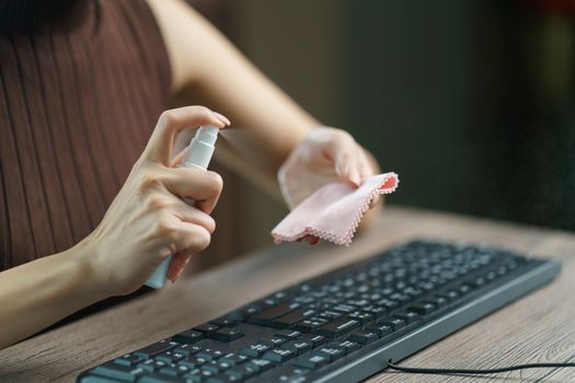 Woman hand desinfecting devices at home for prevent disease by sanitazing keybord, corona virus or Covid-19 protection.