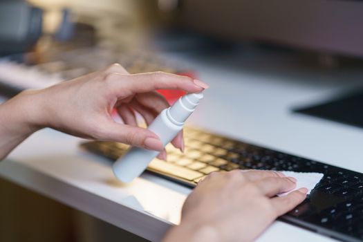 Woman hand desinfecting devices at home for prevent disease by sanitazing keybord, corona virus or Covid-19 protection.