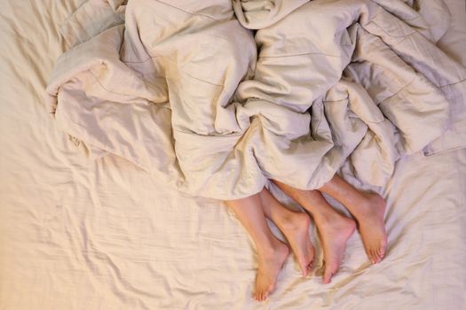 Close up of male and female feet on a bed having sex under sheets in the bedroom.