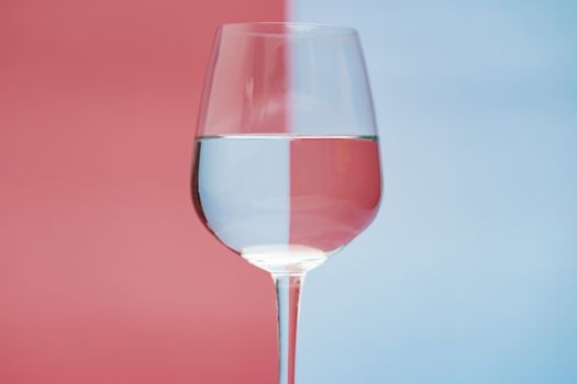 Transparent glass of water, clean drinking water in a clear glass on two tone (pink and blue) background
