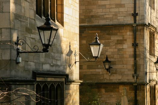 Victorian style street lighting lanterns against Oxford College in afternoon sun. Beautiful image of old fashioned lanterns as street lighting against honey coloured stone of Oxford college. Late golden sun giving great texture and shadows and illuminating lanterns High quality photo