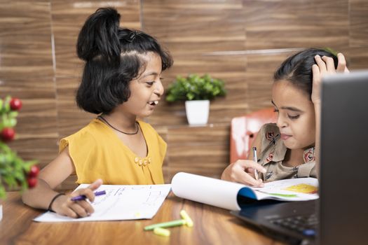 Two kid siblings busy in talking during e-learning or online class - concept of homeschooling or remote classroom at home during covid-19 or coronavirus pandemic lock down