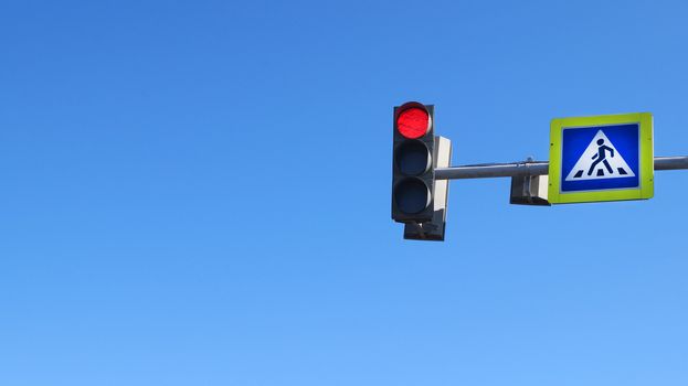 crosswalk sign and red traffic light on blue sky background, copy space.