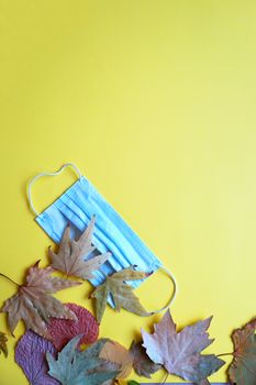 medical mask and autumn leaves on yellow background, copy space, mockup blank