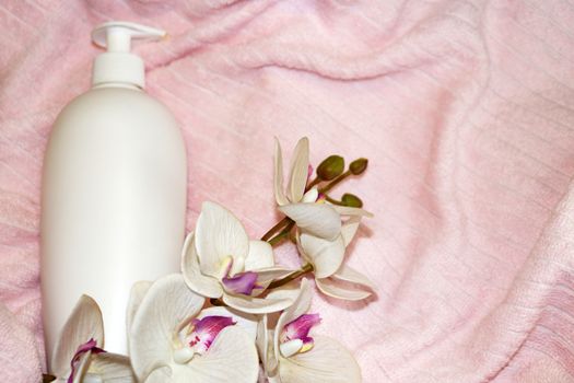 white cosmetic bottle and white orchid flower on pink terry cloth close up