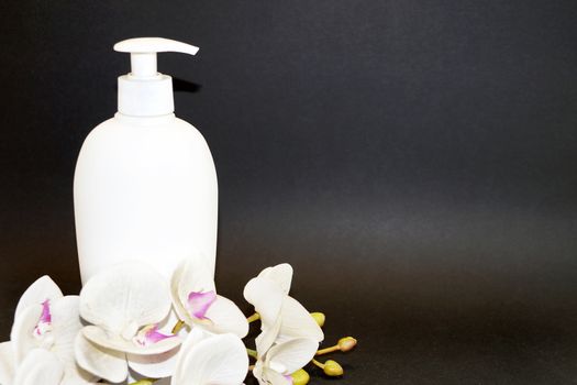 white cosmetic bottle and white orchid flower on a black background close up