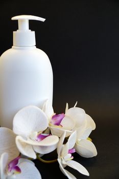 white cosmetic bottle and white orchid flower on a black background close up