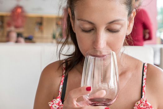 Closeup portrait of young woman with ponytail drinking red wine. Leisure, drinks, degustation, people and holidays concept. Defocused blurry background.