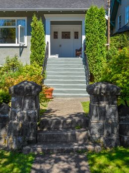Concrete pathway to residential house entrance via landscaped front yard with hedgerows by sides