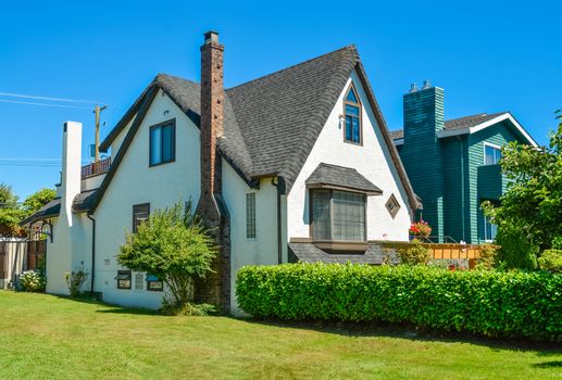 Old style family house with green lawn and hedgerow in front on blue sky background