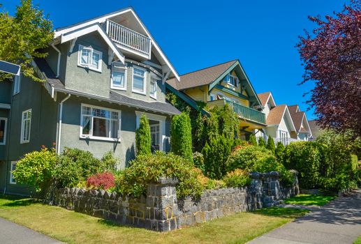A row of residential houses along the street with landscaped front yards. Family houses on sunny day in British Columbia