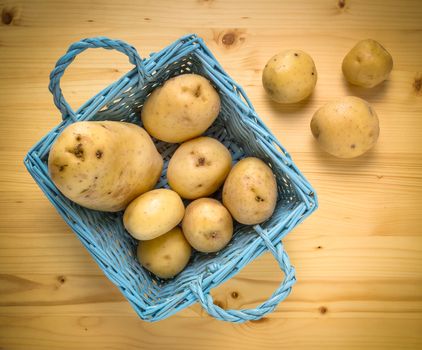 Fresh potatoes in wooden vintage basket on old table as background. Top view