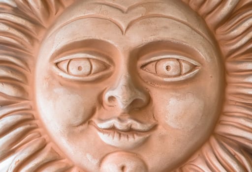 Smiling terracotta sun face. Closeup.