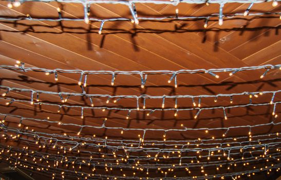 Festive background decorations, garlands of light bulbs on the dark wooden ceiling of the interior. Atmospheric interior decoration in rustic style for the holidays.