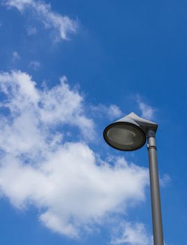 Close - up of modern street lamp of round shape on a blue sky with some white clouds. Space for text.