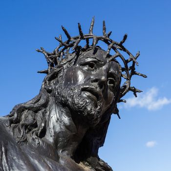 Black statue of Jesus Christ with crown of thorns, in a blue sky background.