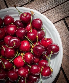 Fresh ripe cherries in a white plate on wood table. Overhead view. Close up.