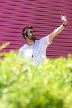 Bearded guy with sunglasses taking a selfie against pink wall