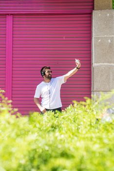 Bearded guy with sunglasses taking a selfie against pink wall
