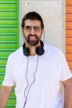 Portrait of a beaded guy with sunglasses and headphones on neck while looking camera