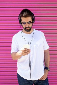 Bearded guy with headphones and sunglasses using a smartphone while listening music