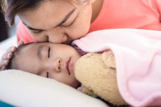 Close up  asian mother kissing  her baby girl Sleeping on the bed. Mother's love and family concept.Side view