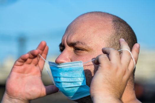 Young man with medical protective face mask illustrates pandemic coronavirus disease on blurred background. SARS-CoV-2 outbreak in Europe. Changes and complications caused by epidemic