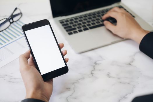 Closeup hands using smartphone mockup at the office desk. Blank screen mobile phone for graphic display montage.