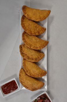 Golden Crispy Empenadas on a Long Plate on a White Background