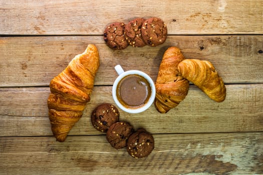 Fresh croissant, puff pastry and biscuits on wooden table. Coffee, food and breakfast concept. Desserts, fresh pastries and coffee. Top view and copy space