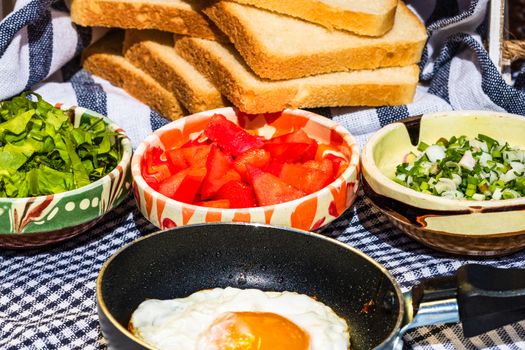 Close up of fried egg in a small frying pan  and different bowls with copped vegetables in a rustic composition