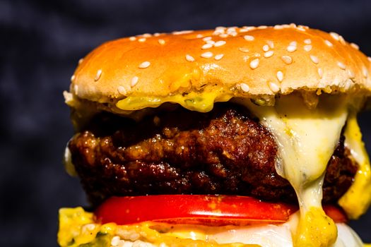 Close up of homemade cheeseburger with onion rings, melted cheese, pickles, tomatoes.