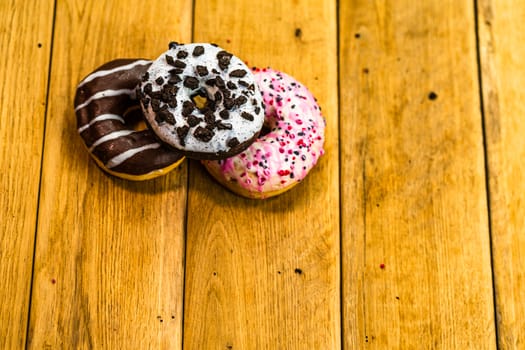 Colorful donuts on wooden table. Sweet icing sugar food with glazed sprinkles, doughnut with chocolate frosting. Top view with copy space