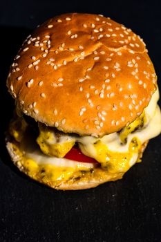 Detail of beef cheeseburger with melted cheese isolated on black background.