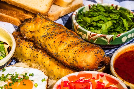 Rustic composition with sausages rolls, fried egg on toast bread, different bowls with sauce and chopped vegetables.