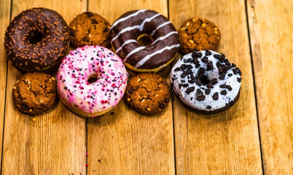 Colorful donuts on wooden table. Sweet icing sugar food with glazed sprinkles, doughnut with chocolate frosting. Top view with copy space