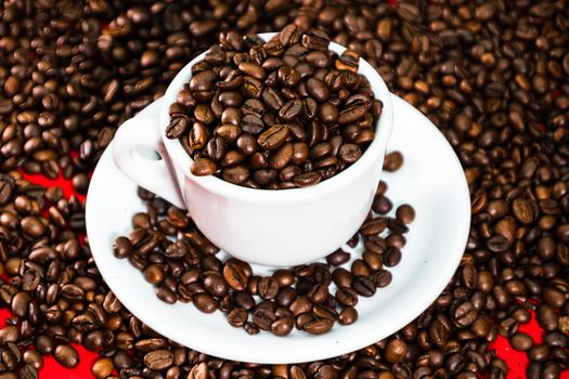 Coffee cup with roasted beans on red and coffee beans background. Close up top view, coffee concept