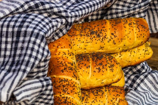 Sausages baked in dough sprinkled with salt and poppy seeds in a rustic basket. Sausages rolls, delicious homemade pastries in a rustic composition.