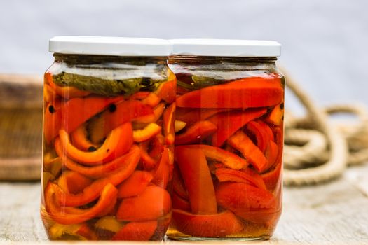 Glass jars with pickled red bell peppers.Preserved food concept, canned vegetables isolated in a rustic composition.