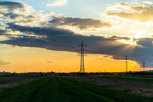 Beautiful dramatic sky and clouds, sunset lights over the transmission tower (electricity pylon) on a field.