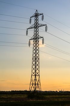 Beautiful dramatic sky and clouds, sunset lights over the transmission tower (electricity pylon) on a field.