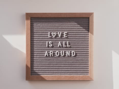 Top view on letter board with words LOVE IS ALL AROUND. Flat lay concept heart symbol of love and romance. Sunlight and shadows.