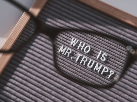 Letterboard with question WHO IS MR.TRUMP? through eyeglasses. Concept of political situation. Social issue. Closer look at the past of the USA President before the elections.