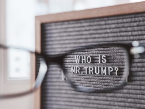 Letterboard with question WHO IS MR.TRUMP? through eyeglasses. Concept of political situation. Social issue. Closer look at the past of the USA President before the elections.