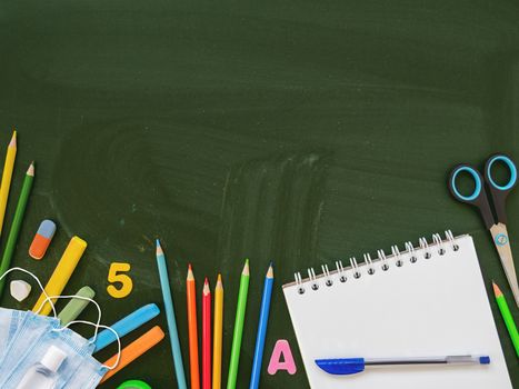 Top view on colorful stationery, protective medical masks and hand sanitizer. Back to school flat lay concept. Horizontal blackboard background with copy space. School shopping. New normal.