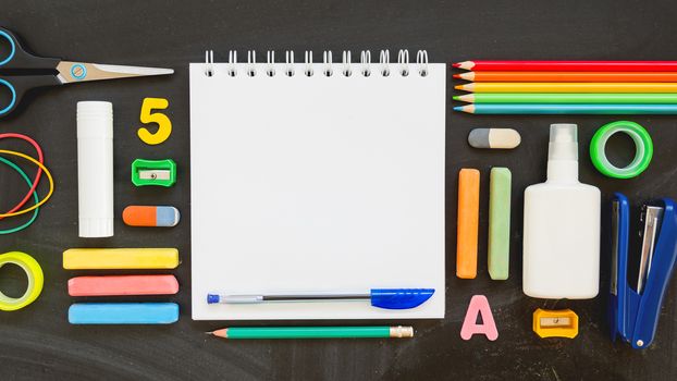 Top view on colorful stationery. Back to school flat lay concept. Horizontal 16:9 blackboard background with copy space on notepad.