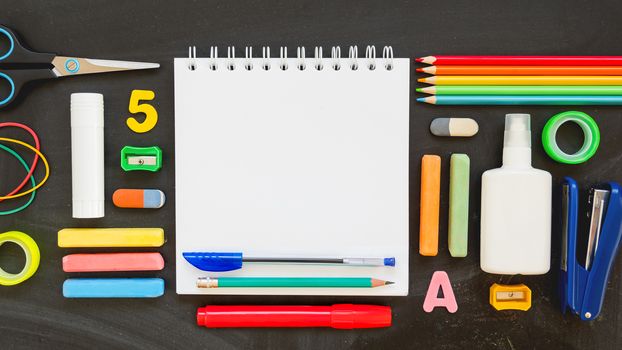 Top view on colorful stationery. Back to school flat lay concept. Horizontal 16:9 blackboard background with copy space on notepad.