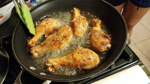 chicken drumsticks cooking in hot oil in frying pan on stove