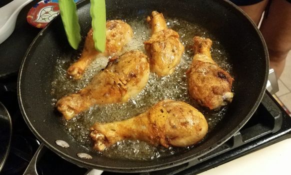 chicken drumsticks cooking in hot oil in frying pan on stove